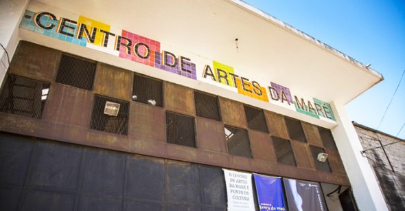 Fachada do Centro de Artes da Maré com letreiro em mosaico colorido sobre estrutura metálica e cartazes culturais na entrada